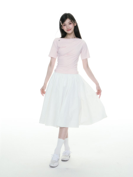 Woman modeling a light pink top with a white midi skirt on a white background