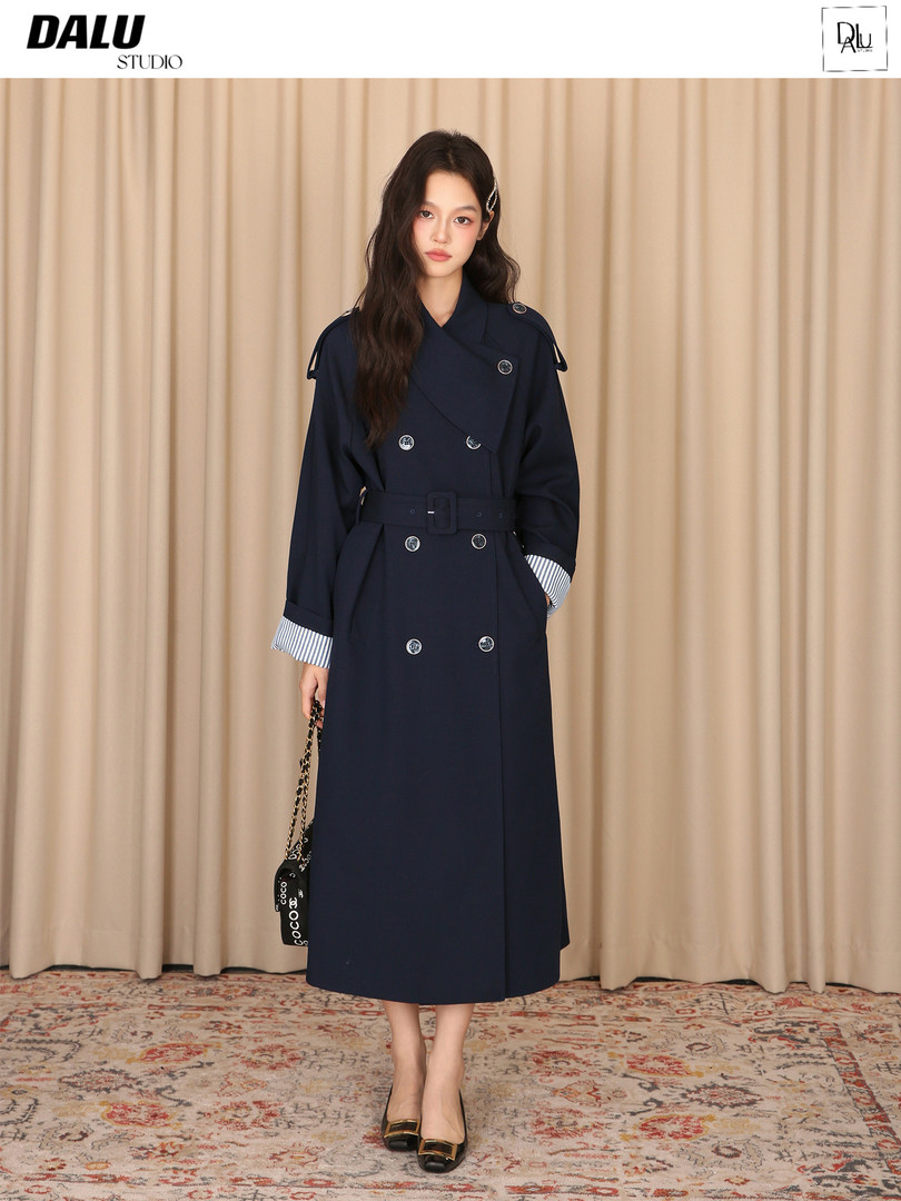 Model wearing a navy double-breasted long trench coat with belt
