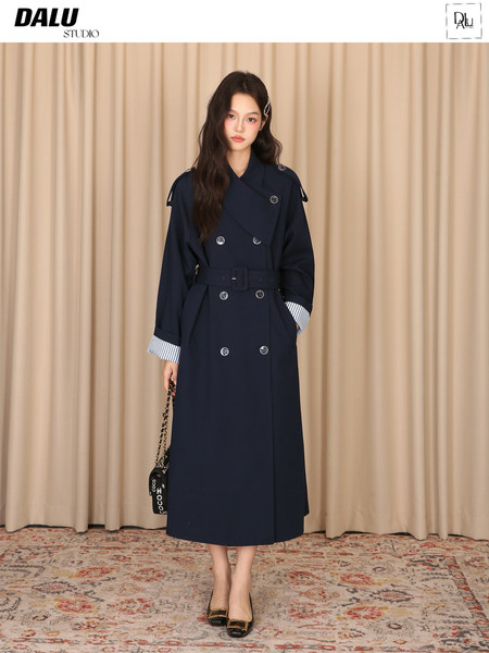 Model wearing a navy double-breasted long trench coat with belt