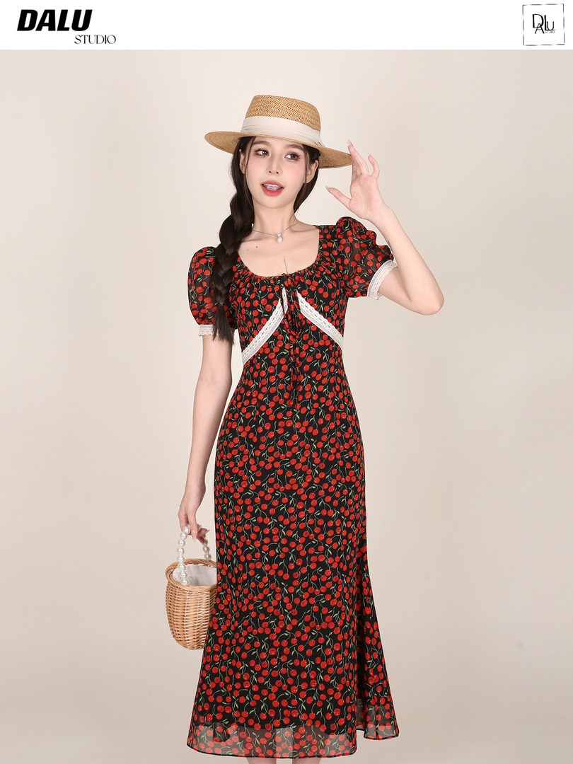 Model wearing a black cherry-print dress with a straw hat and wicker bag