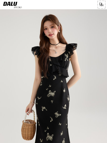 Model wearing a black butterfly-print ruffled dress with a woven handbag