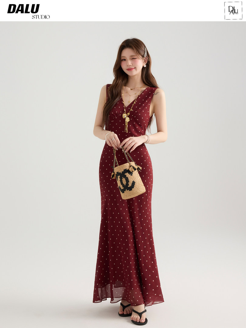 Model wearing a burgundy polka dot maxi dress with a woven handbag