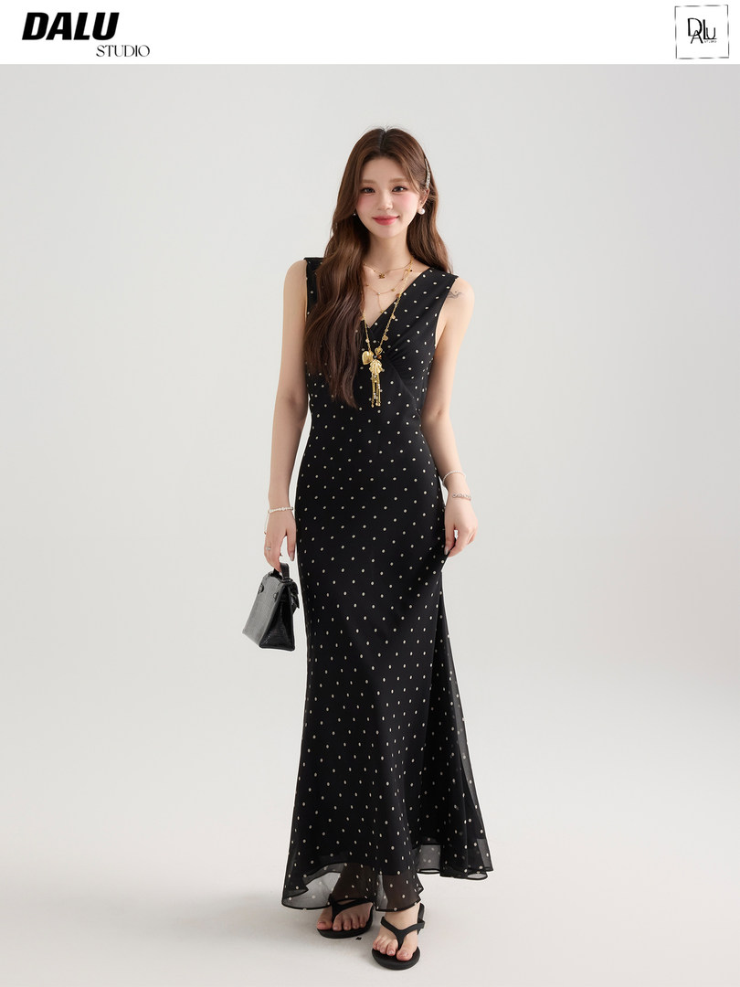 Woman wearing a black polka dot sleeveless maxi dress with a small handbag