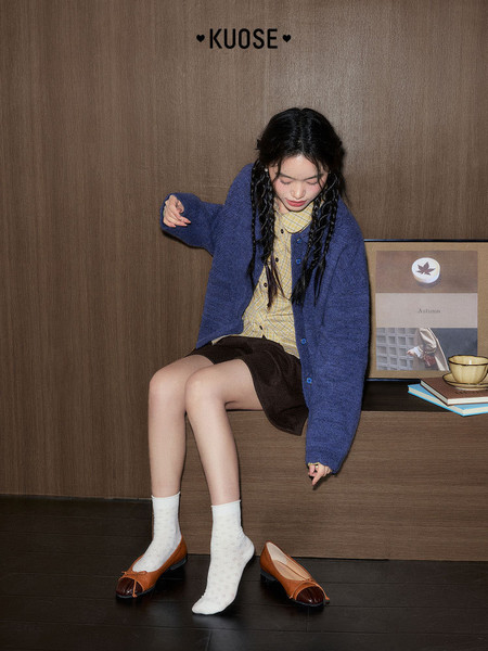 Model wearing a blue cardigan with a yellow blouse, skirt, socks, and brown loafers