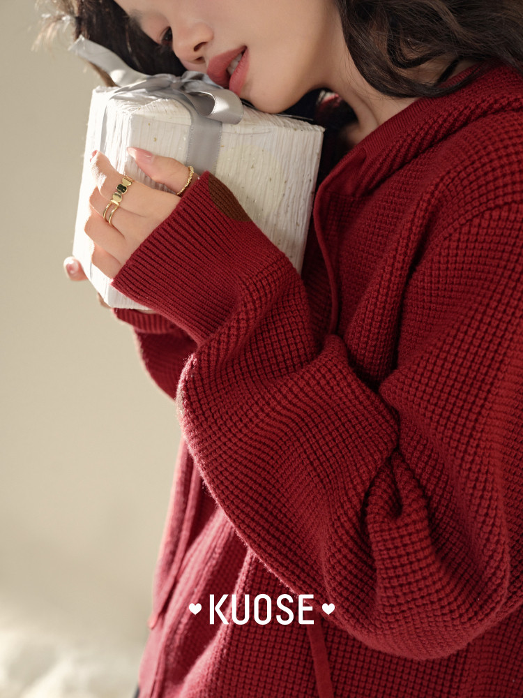 Model wearing a red knit hoodie sweater and holding a white gift box