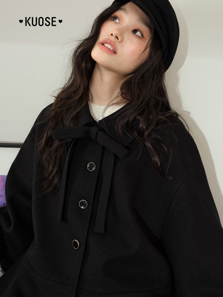Black coat worn by a model with bow tie detail and button front