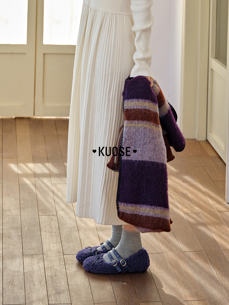 Model wearing a cream pleated dress with a striped scarf and purple fuzzy shoes