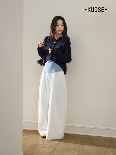 Model wearing a navy top with wide white pants and a small handbag