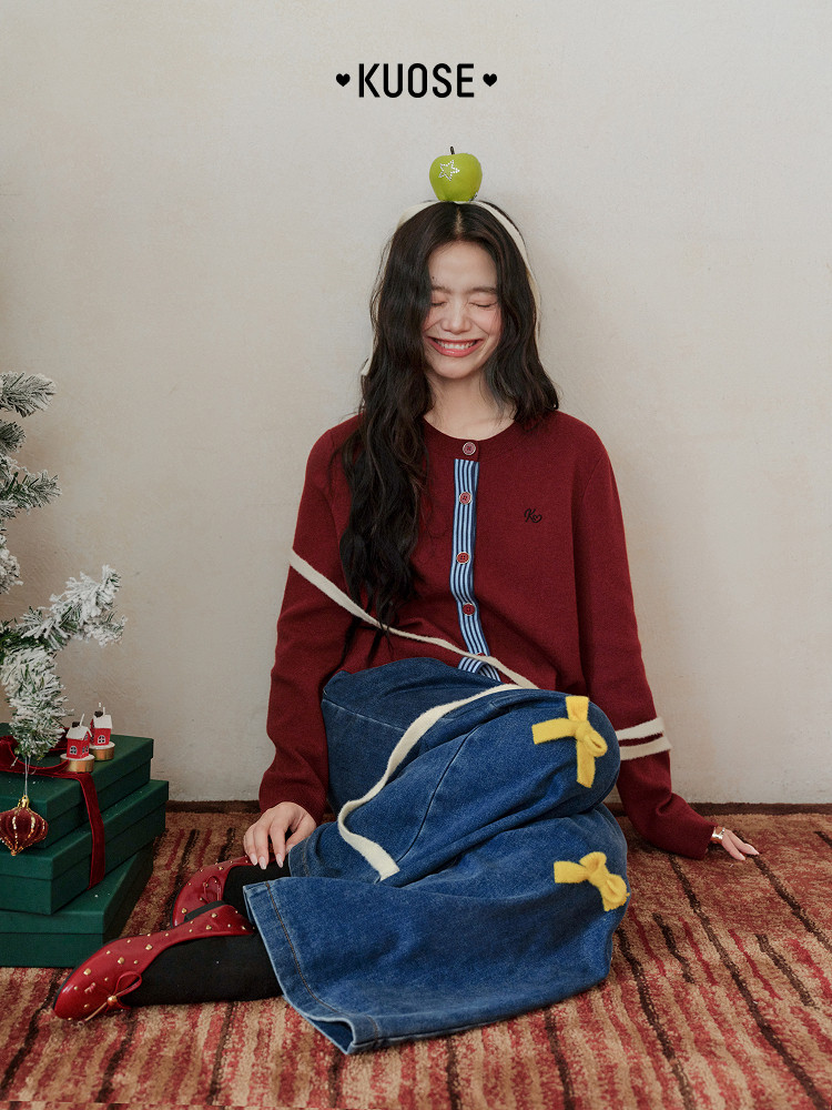 Woman wearing a red knit cardigan and blue denim skirt in a festive holiday setting