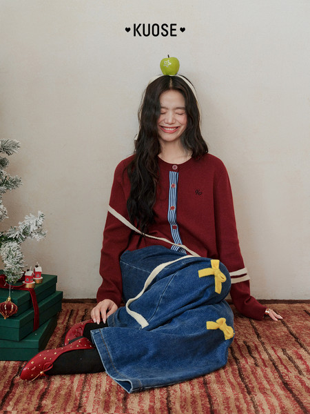 Woman wearing a red knit cardigan and blue denim skirt in a festive holiday setting