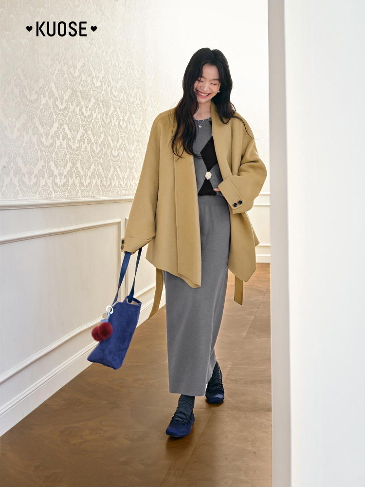 Woman wearing a camel coat with a gray skirt and blue bag