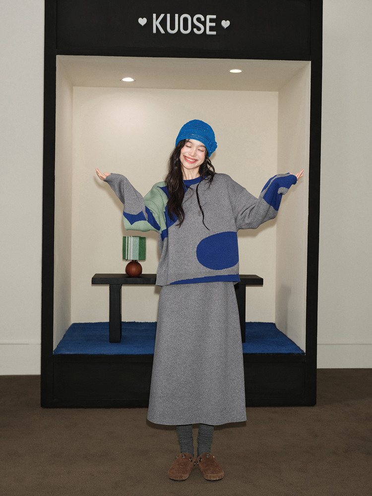 Model wearing a gray and blue knit sweater set with matching skirt and beanie