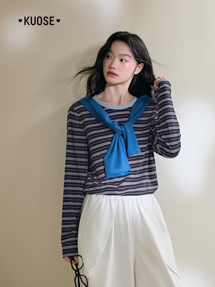 Model wearing a navy striped long-sleeve top with a blue sweater draped over the shoulders and white pants