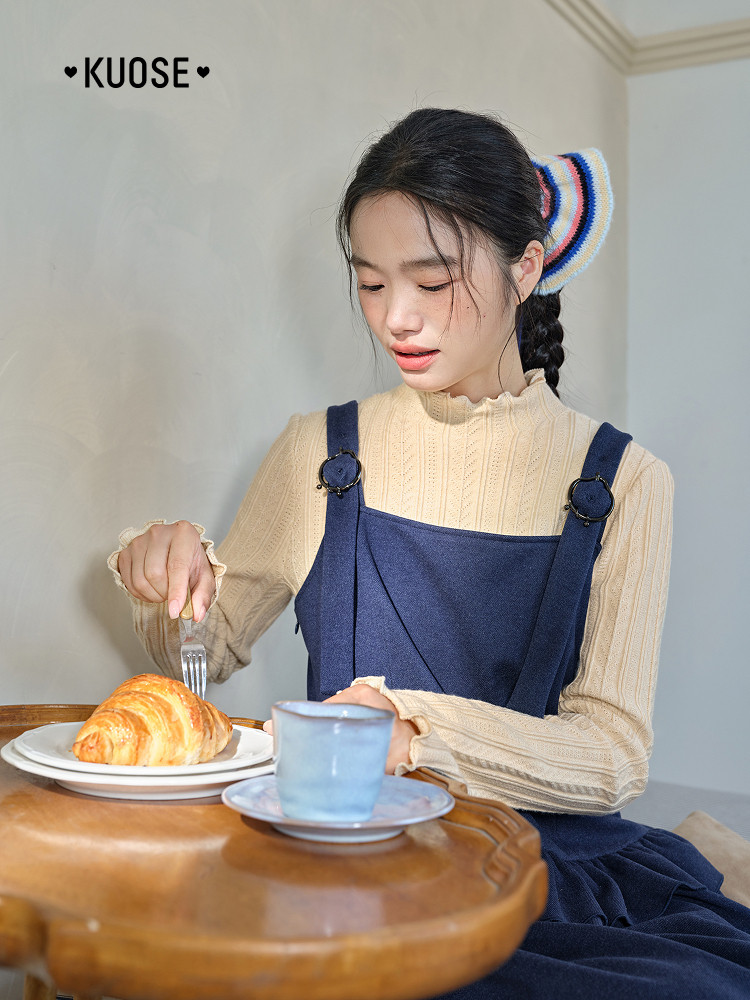 Woman wearing a beige textured top with a navy pinafore dress at a table