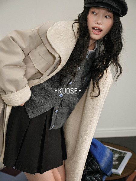 Model wearing a beige shearling-lined coat over a gray cardigan and black skirt