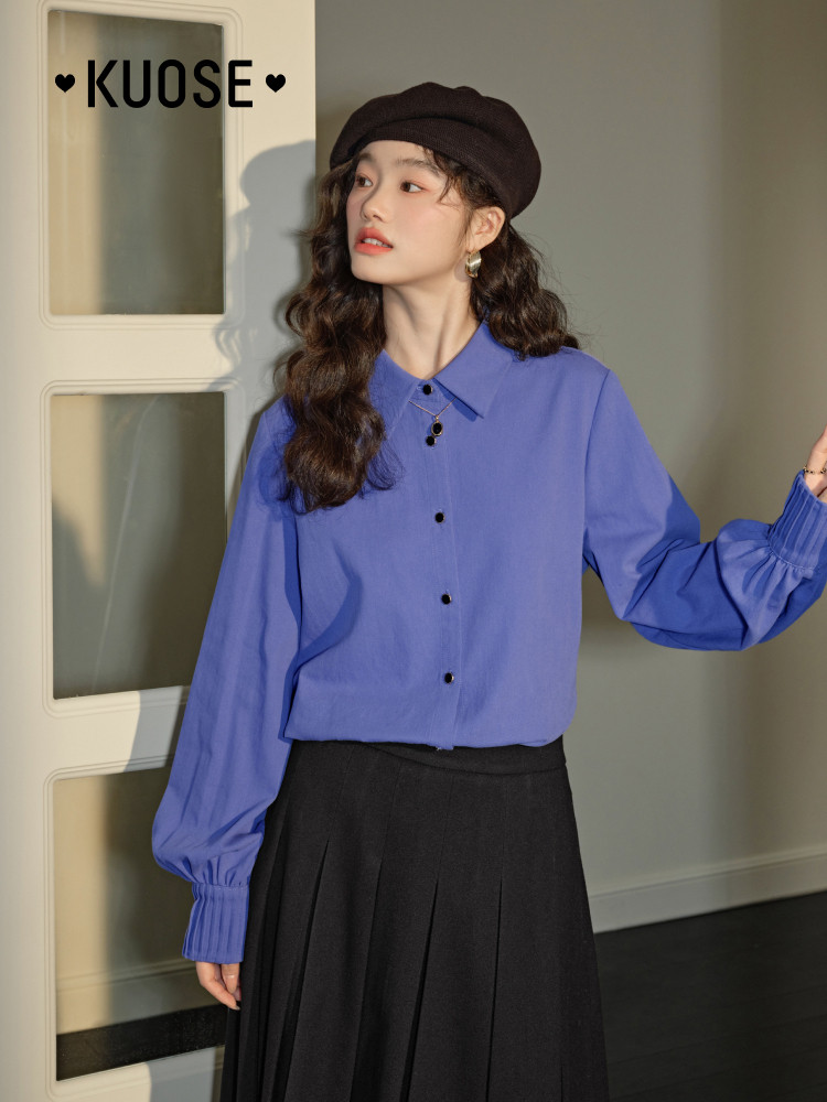 Woman wearing a blue button-up blouse with a black skirt and beret