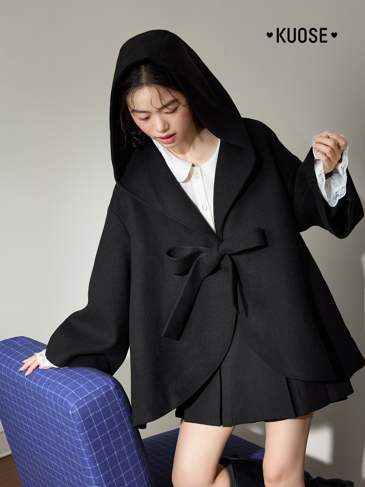 Black hooded wrap coat worn by a model over a white top and skirt