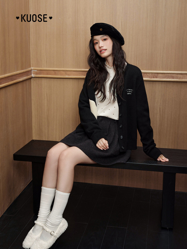 Fashion model wearing a black cardigan, skirt, beret, and white socks indoors