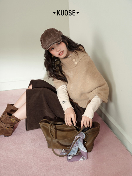 Model wearing a beige knit top with brown skirt, cap, boots, and a handbag