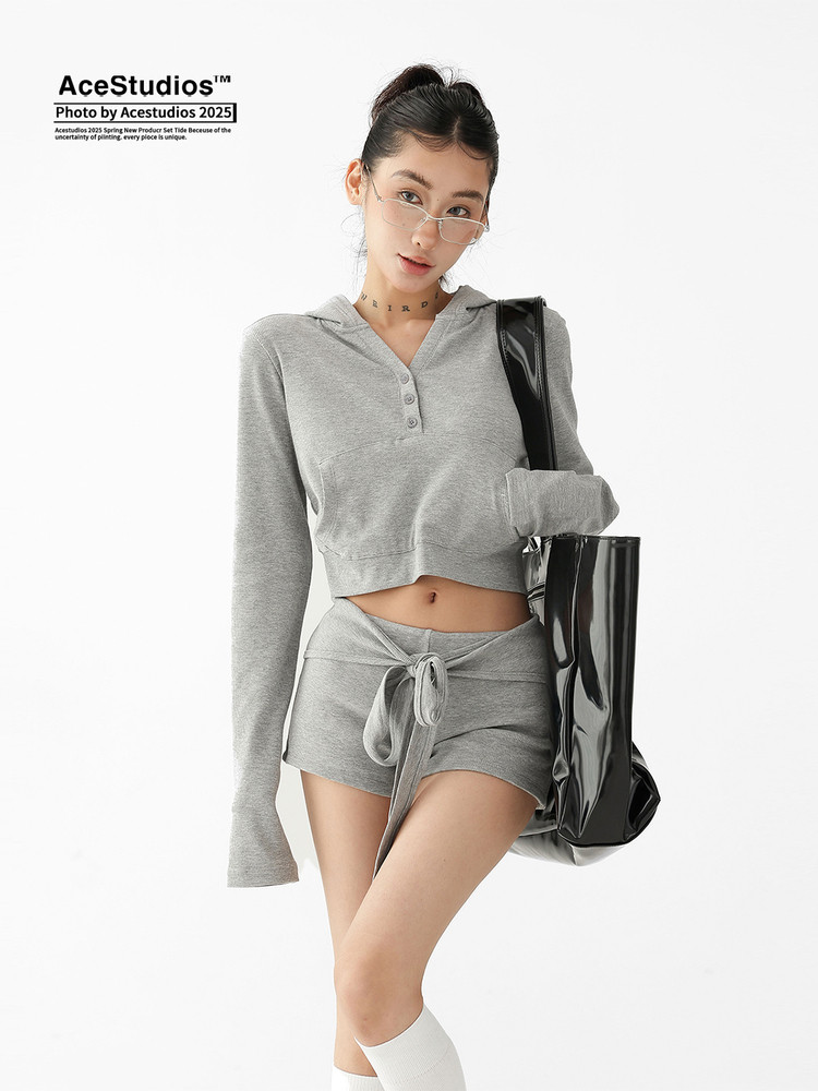 Model wearing a gray cropped hoodie and matching mini skirt set with a black tote bag