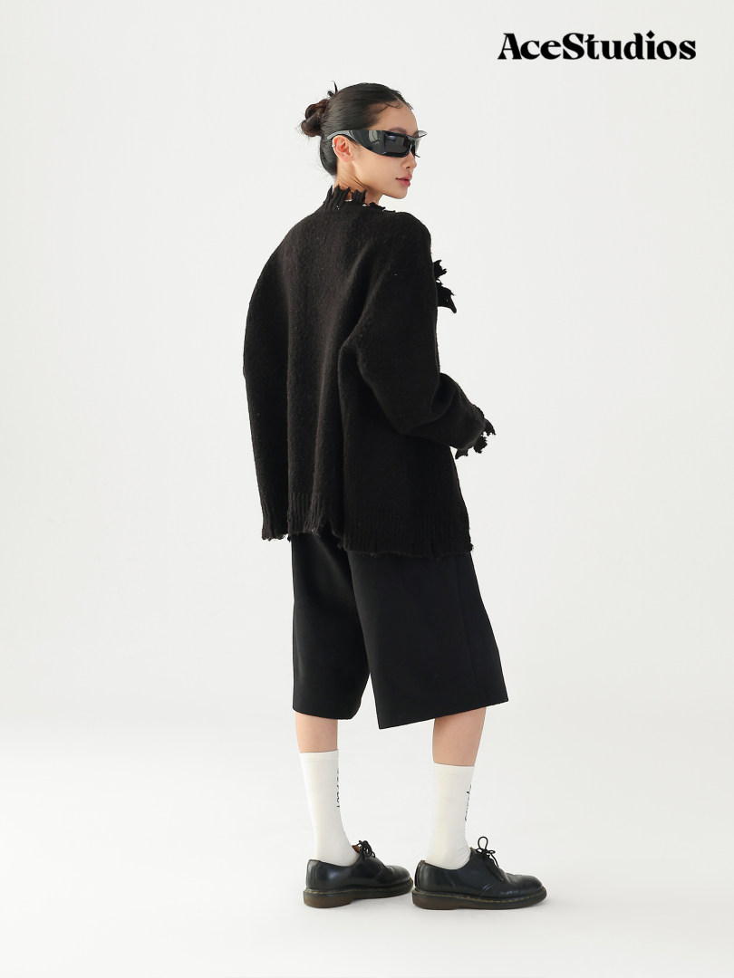 Model wearing a black oversized knit top with wide shorts, socks, and black shoes