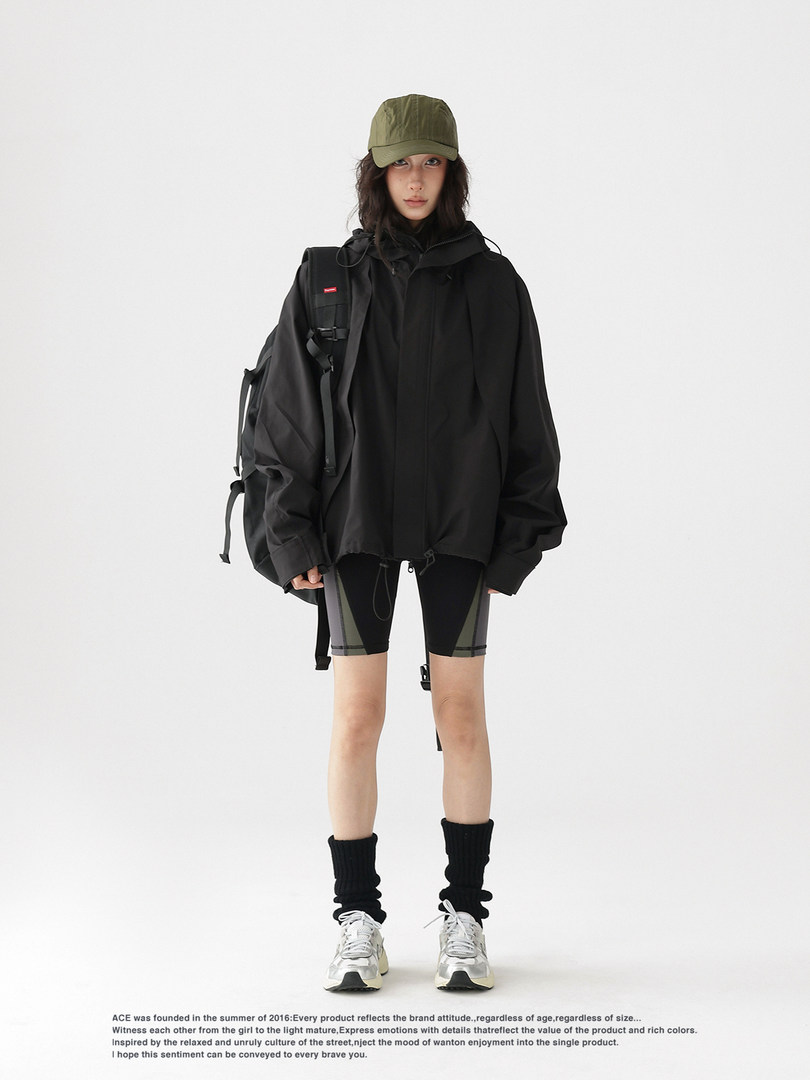 Model wearing a black oversized hooded jacket with shorts, cap, and sneakers