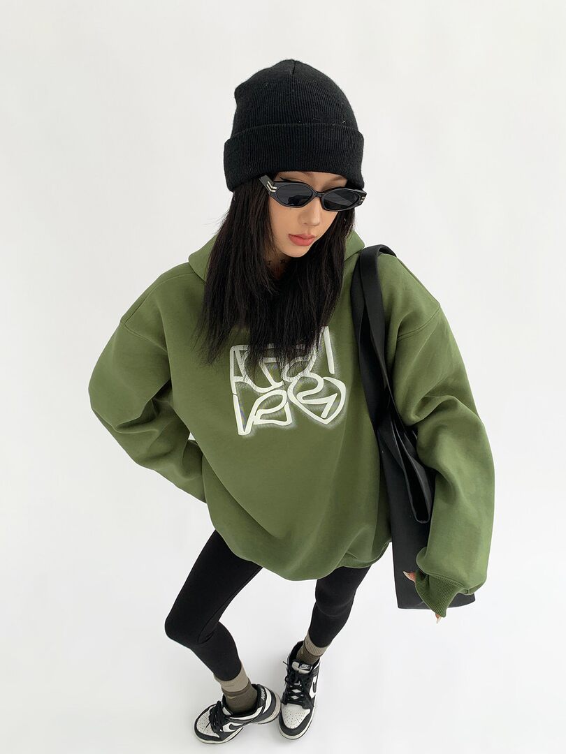 Model wearing an oversized olive green hoodie with black beanie and sneakers
