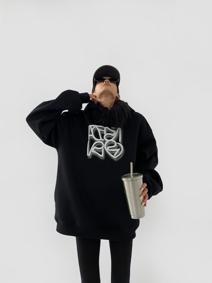 Black oversized graphic hoodie worn by a model holding a tumbler