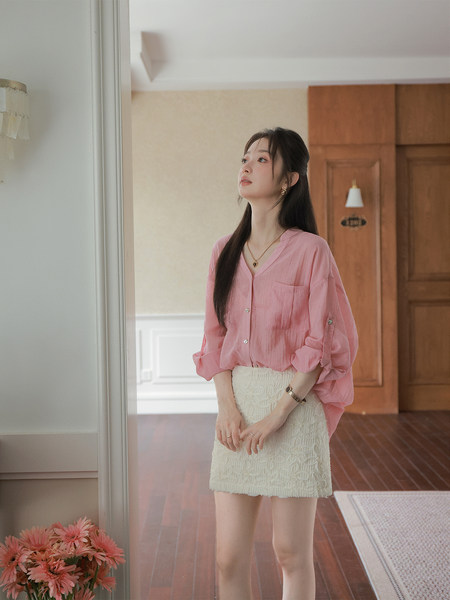 Model wearing a pink blouse with a white textured mini skirt indoors