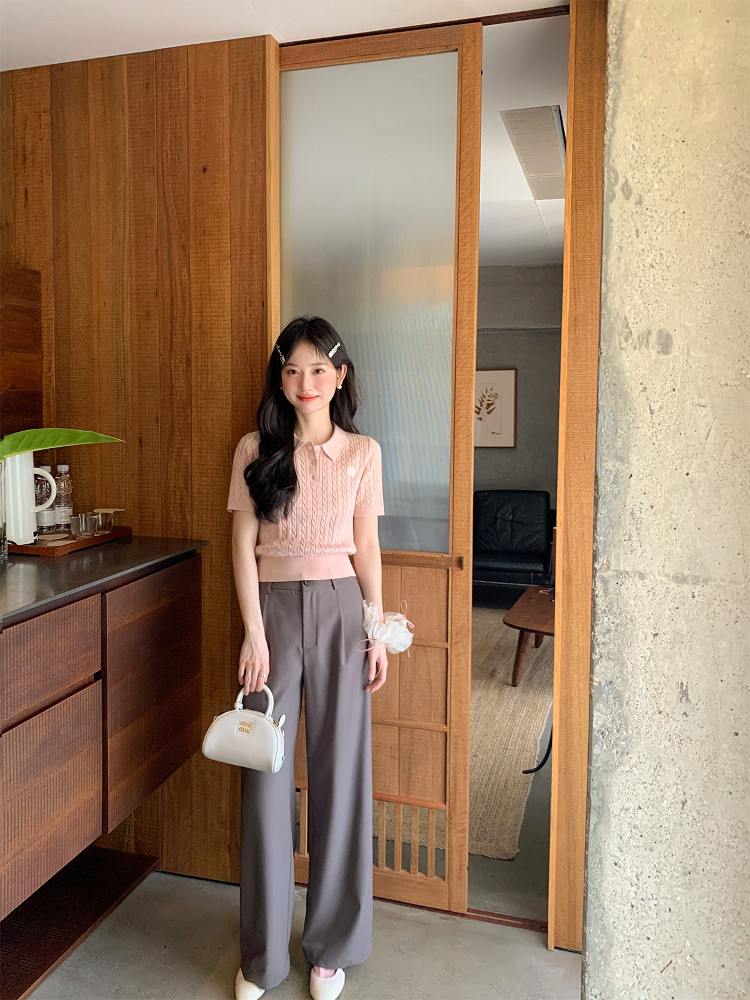 Woman modeling a pink short-sleeve knit top with gray wide-leg trousers and a small handbag