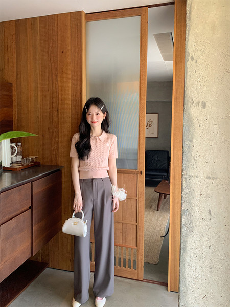 Woman modeling a pink short-sleeve knit top with gray wide-leg trousers and a small handbag