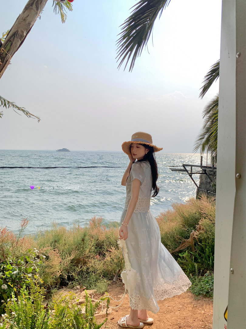 Woman wearing a light lace dress and straw hat by the seaside