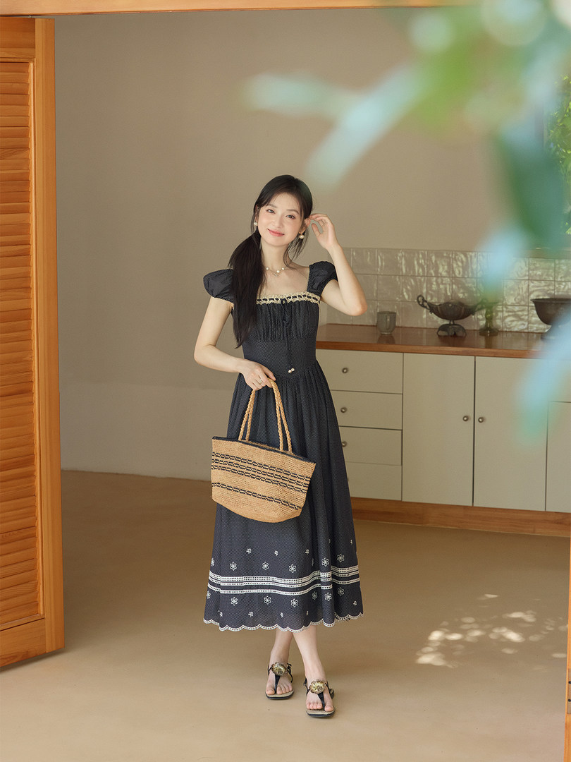 Woman wearing a black patterned summer dress and holding a straw tote bag