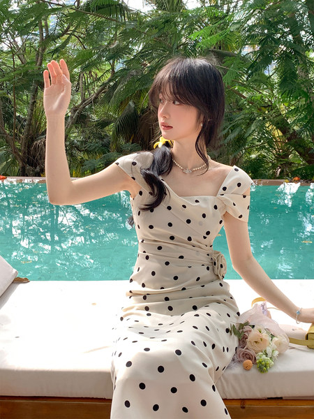 Woman wearing a cream polka dot dress by a pool