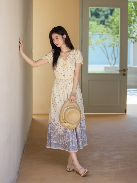 Woman wearing a cream and lavender floral midi dress holding a straw hat