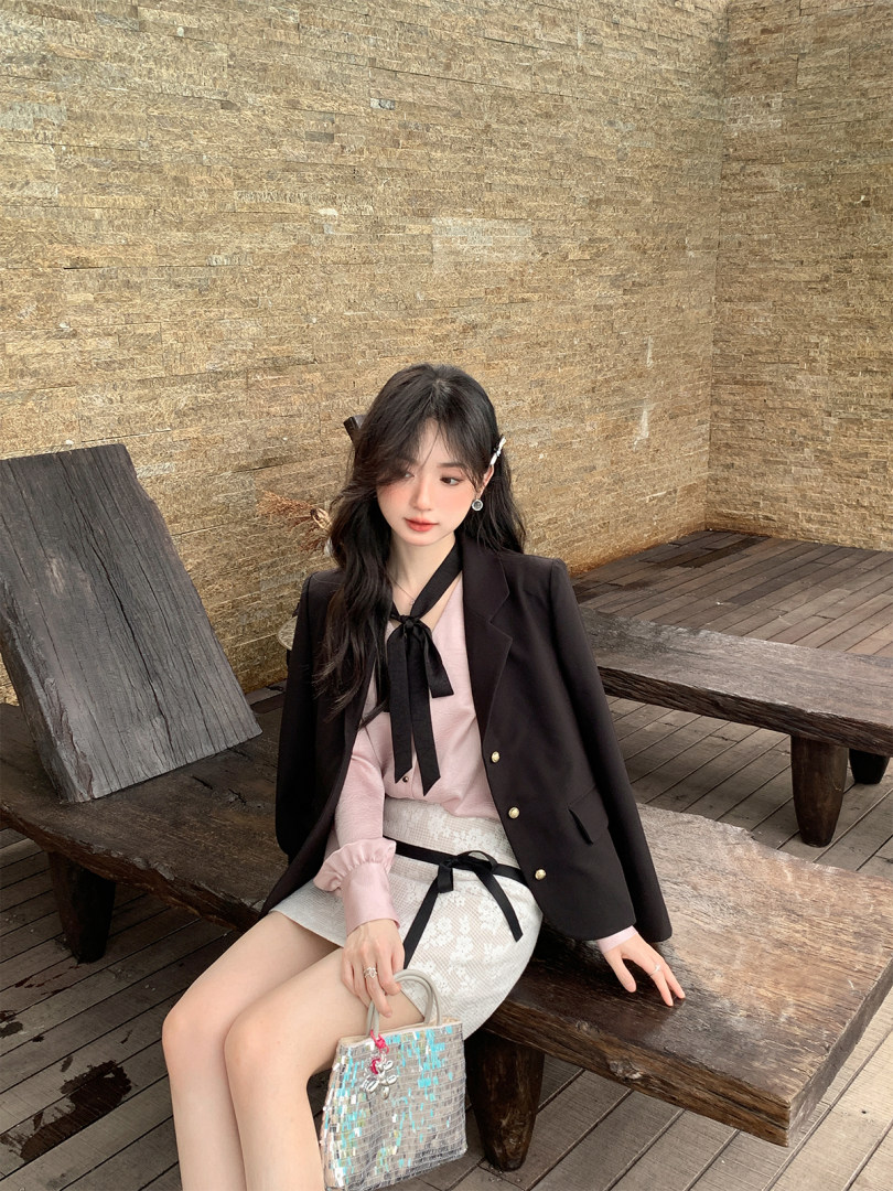 Fashion model wearing a black blazer with a pink blouse, white skirt, and matching handbag