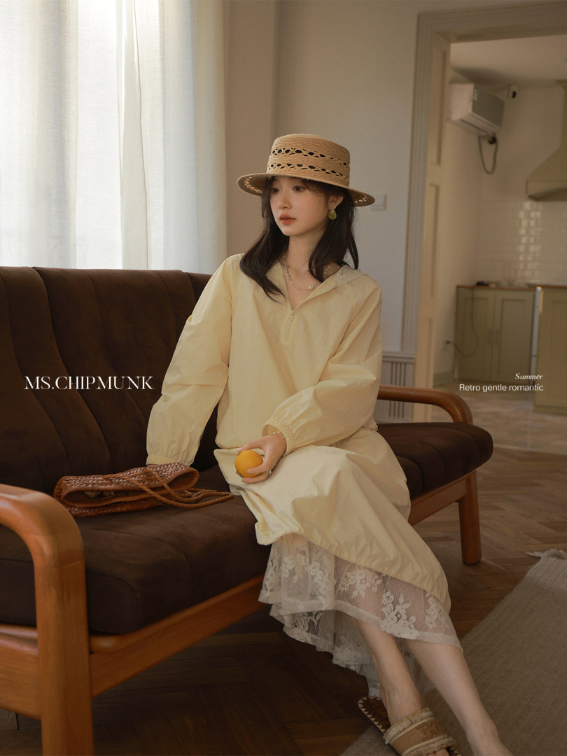 Woman wearing a cream long-sleeve dress and straw hat sitting on a sofa