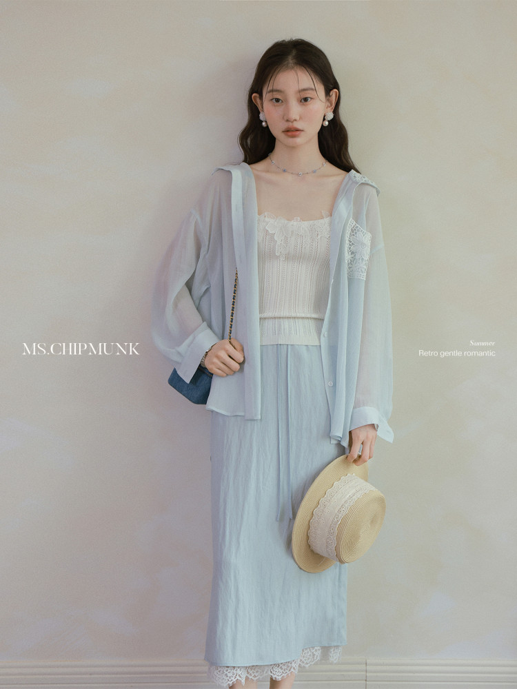 Model wearing a light blue sheer blouse and matching skirt set with a straw hat.