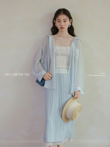 Model wearing a light blue sheer blouse and matching skirt set with a straw hat.