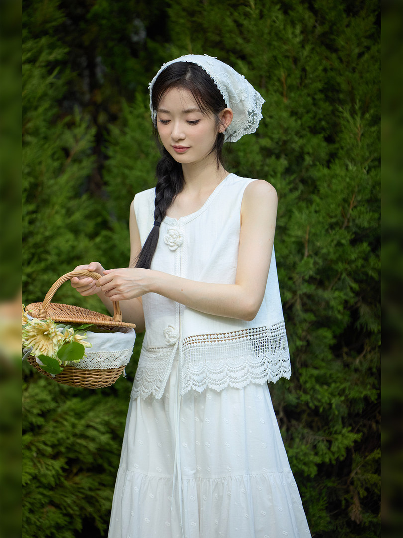 Woman wearing a white lace sleeveless dress and vest outdoors holding a wicker basket