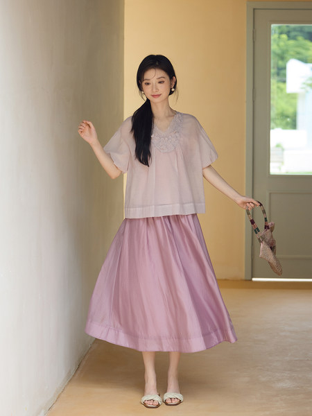 Model wearing a light pink blouse and matching skirt with sandals