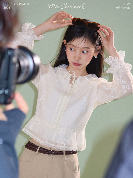 Model wearing a sheer white lace blouse with long sleeves and a tie neckline