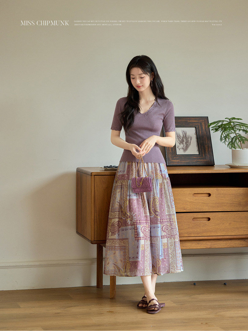 Model wearing a purple ribbed short-sleeve top with a patterned midi skirt and small handbag