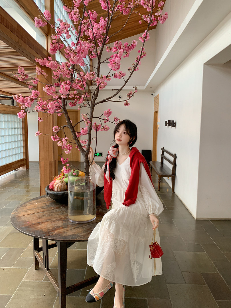 Woman wearing a white long-sleeve dress with a red sweater in a cherry blossom setting