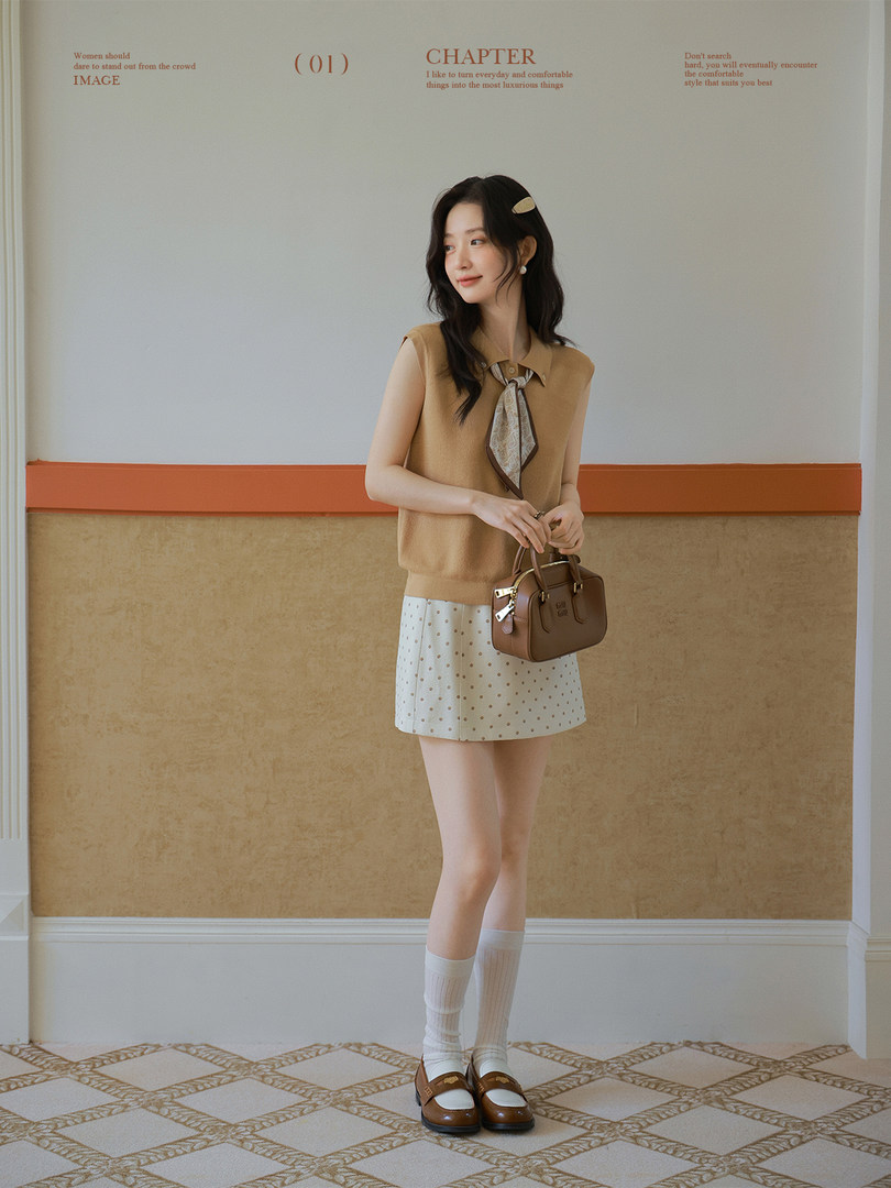 Woman wearing a tan sleeveless top and polka dot mini skirt with loafers and a handbag