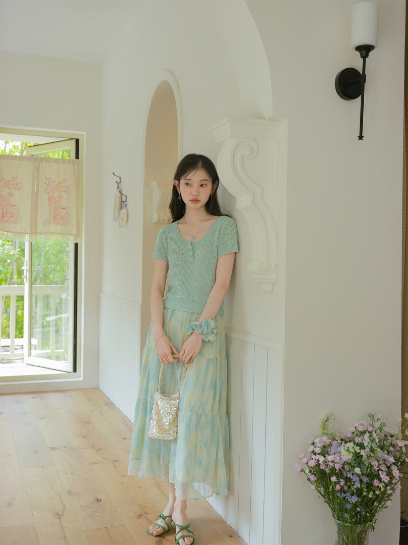 Model wearing a light green knit top and pastel tiered skirt in a bright room