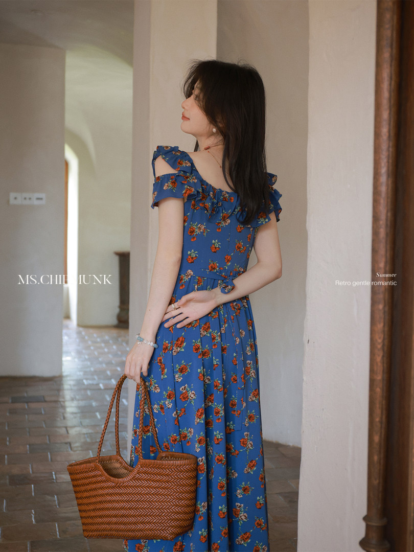 Woman wearing a blue floral ruffle dress and holding a woven tote bag