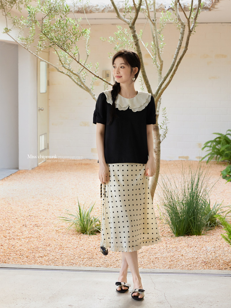 Model wearing a black top with a white ruffled collar and a cream polka dot skirt