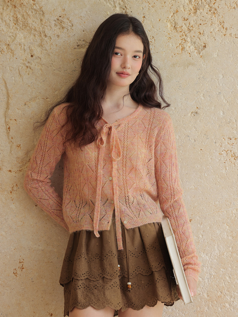 Model wearing a peach sheer knit cardigan with a brown layered skirt