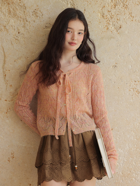 Model wearing a peach sheer knit cardigan with a brown layered skirt